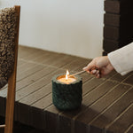 Person lighting a candle in a textured candle holder.