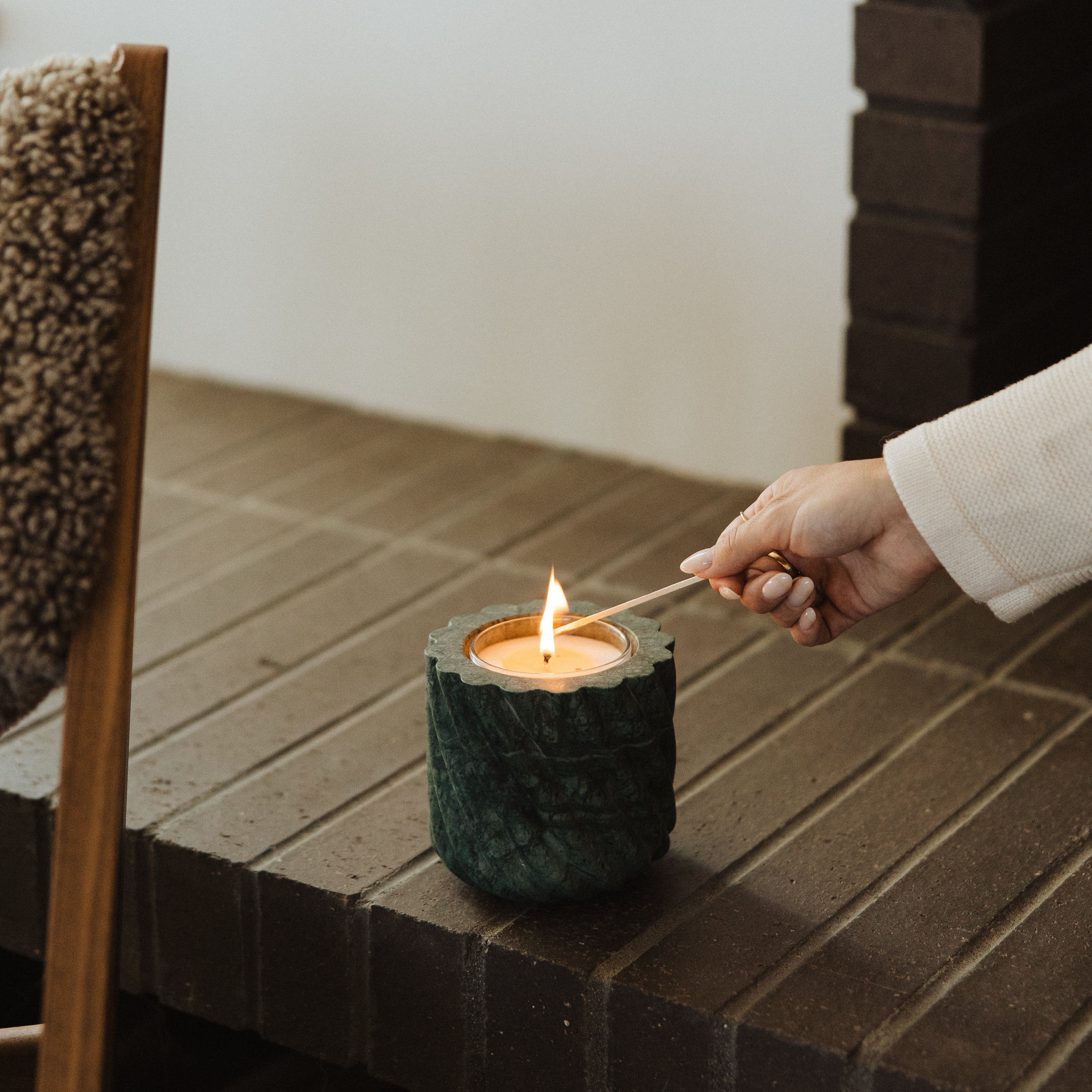 Person lighting a candle in a textured candle holder.