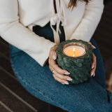Person holding a green textured candle holder with a lit candle inside.